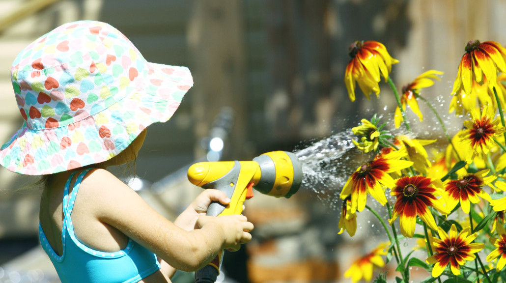 jente i sommerhatt som vanner blomster