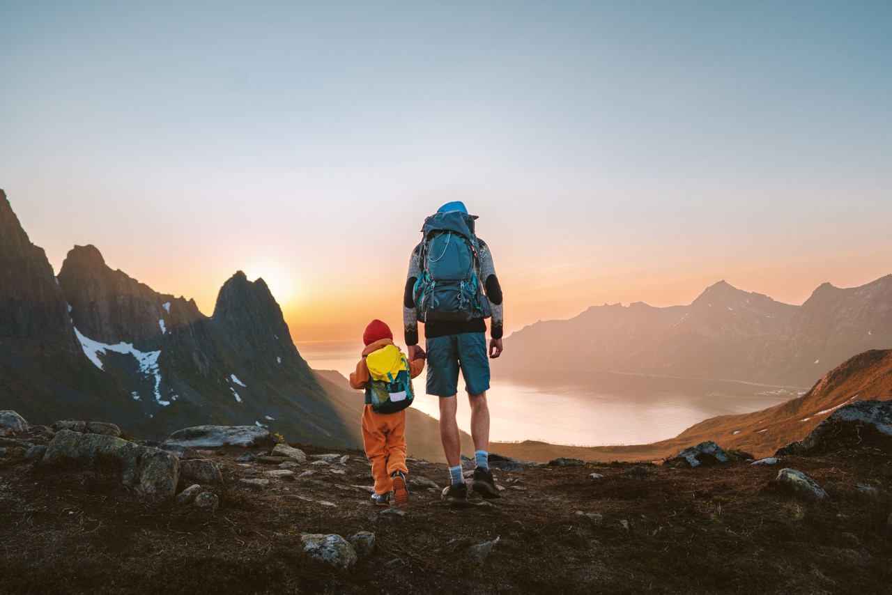 Venstre tar #klimakampen – En far og hans barn står på toppen av et fjell i norsk natur, kledd for fjelltur, og ser utover landskapet med en vakker solnedgang i horisonten. Bildet symboliserer Venstres klima- og miljøpolitikk, med fokus på bærekraft og framtidige generasjoner.